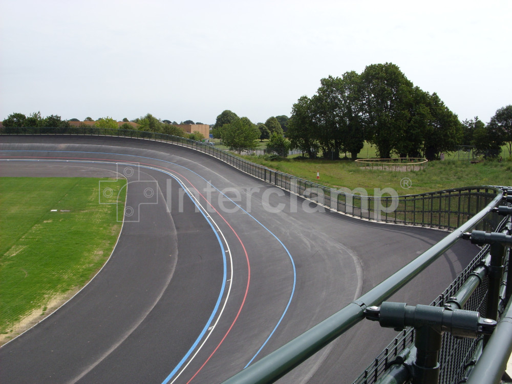 Powder-coated dark green Interclamp tube clamp DDA fittings securing a safety barrier at a velodrome, ensuring a reliable and durable structure for cyclist protection